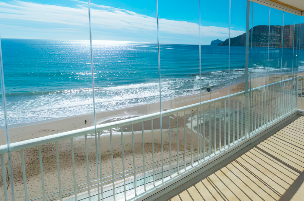 Large floor to ceiling glass curtains installed on balcony overlooking beach and sea below.